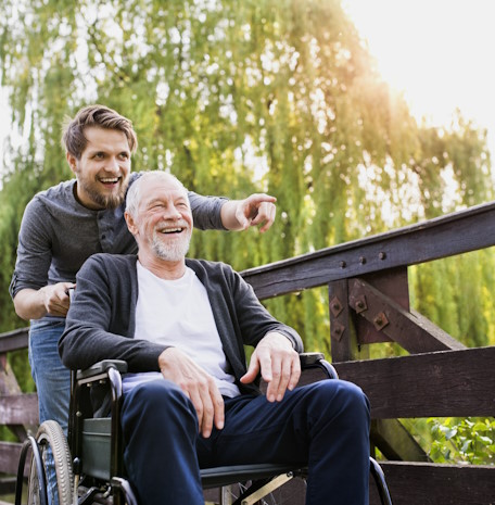 Hipster son walking with disabled father in wheelchair at park.